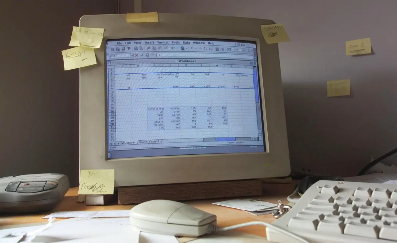 A beige desktop computer showing a spreadsheet, with sticky notes on the monitor